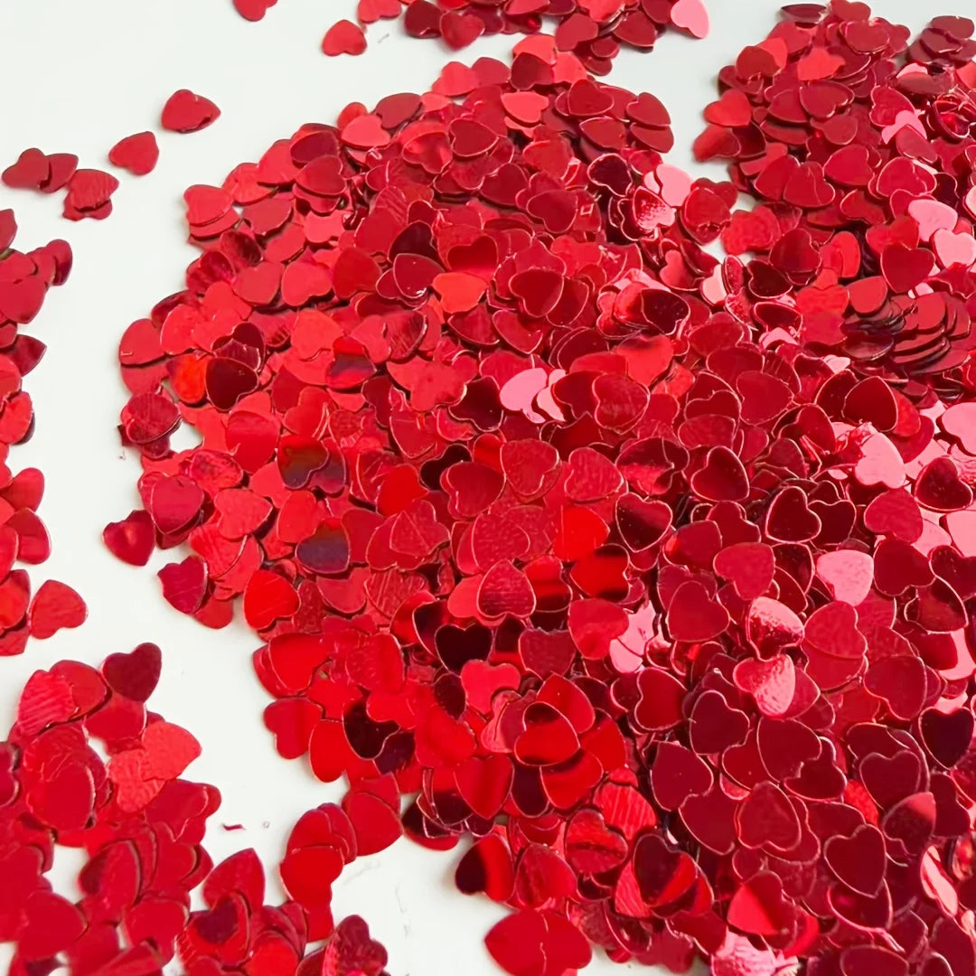 A pile of red heart-shaped foil confetti scattered on a white surface.