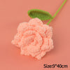 A handmade pink crochet rose flower with a green leaf on a peach background.