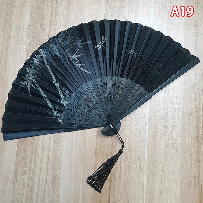 A dark gray folding hand fan with delicate leaf patterns, shown open on a light wooden surface.