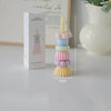 A tall, stacked candle in pastel colors is shown next to its packaging and a measuring scale.