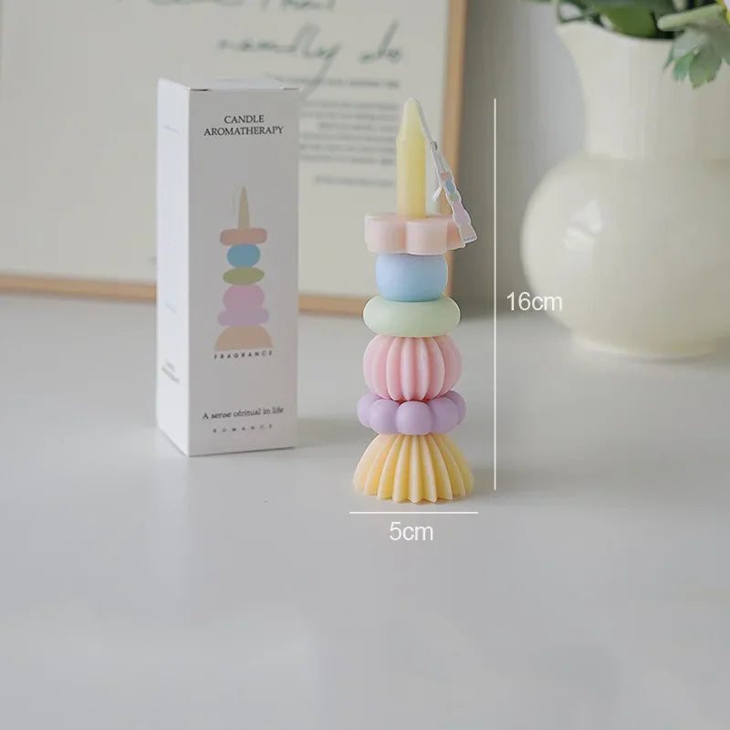 A tall, stacked candle in pastel colors is shown next to its packaging and a measuring scale.