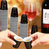 Hands hold mini black plastic shot cups for tastings next to a glass of rosé wine.