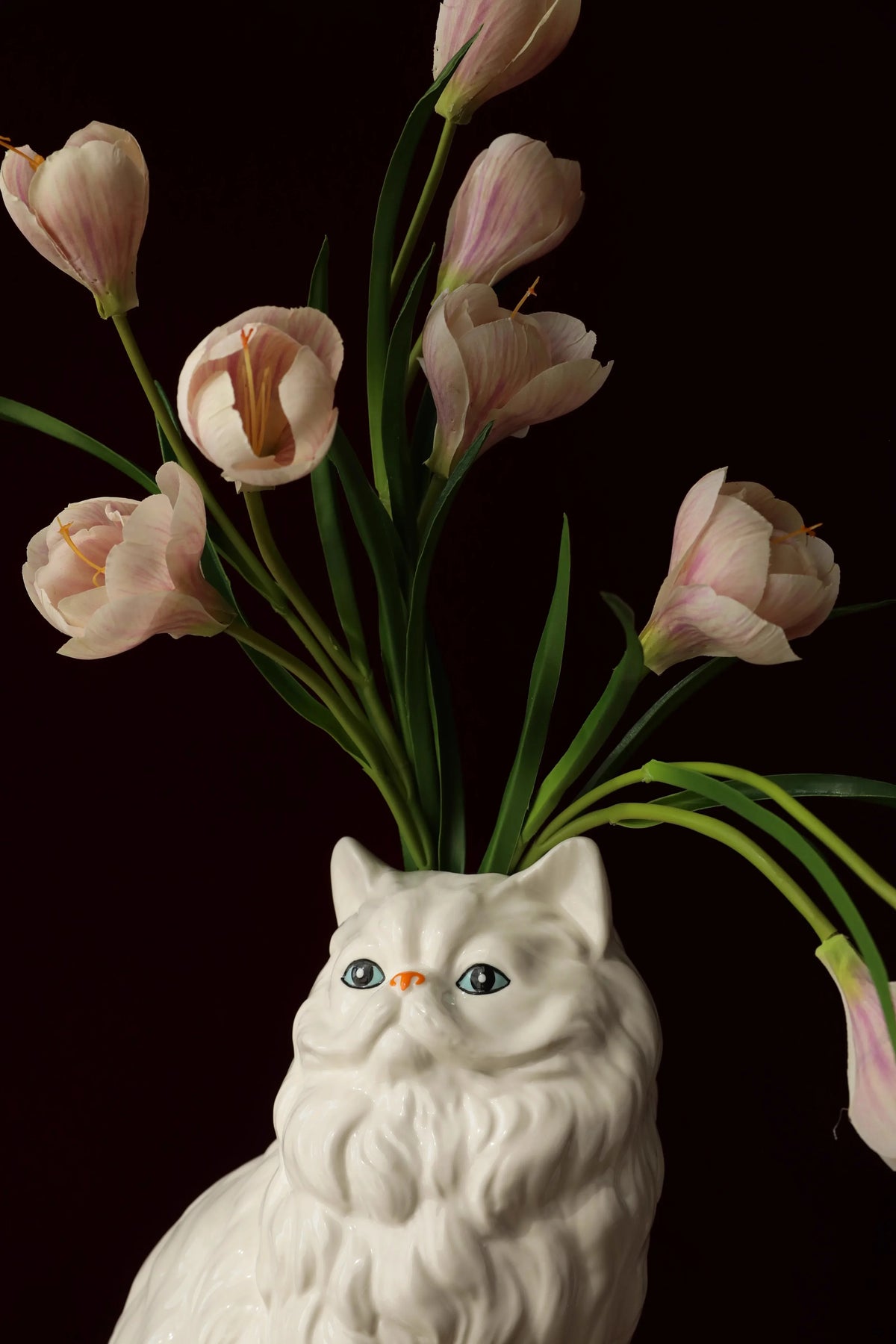 A white ceramic cat sculpture with pink tulips emerging from its form.