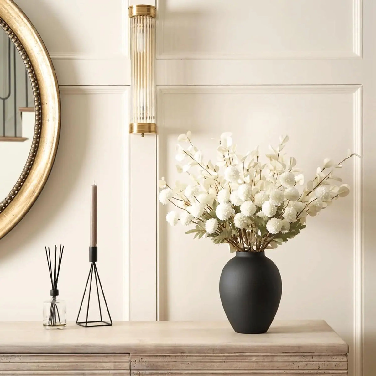 A black ceramic vase filled with white baby's breath flowers sits on a light wooden surface.