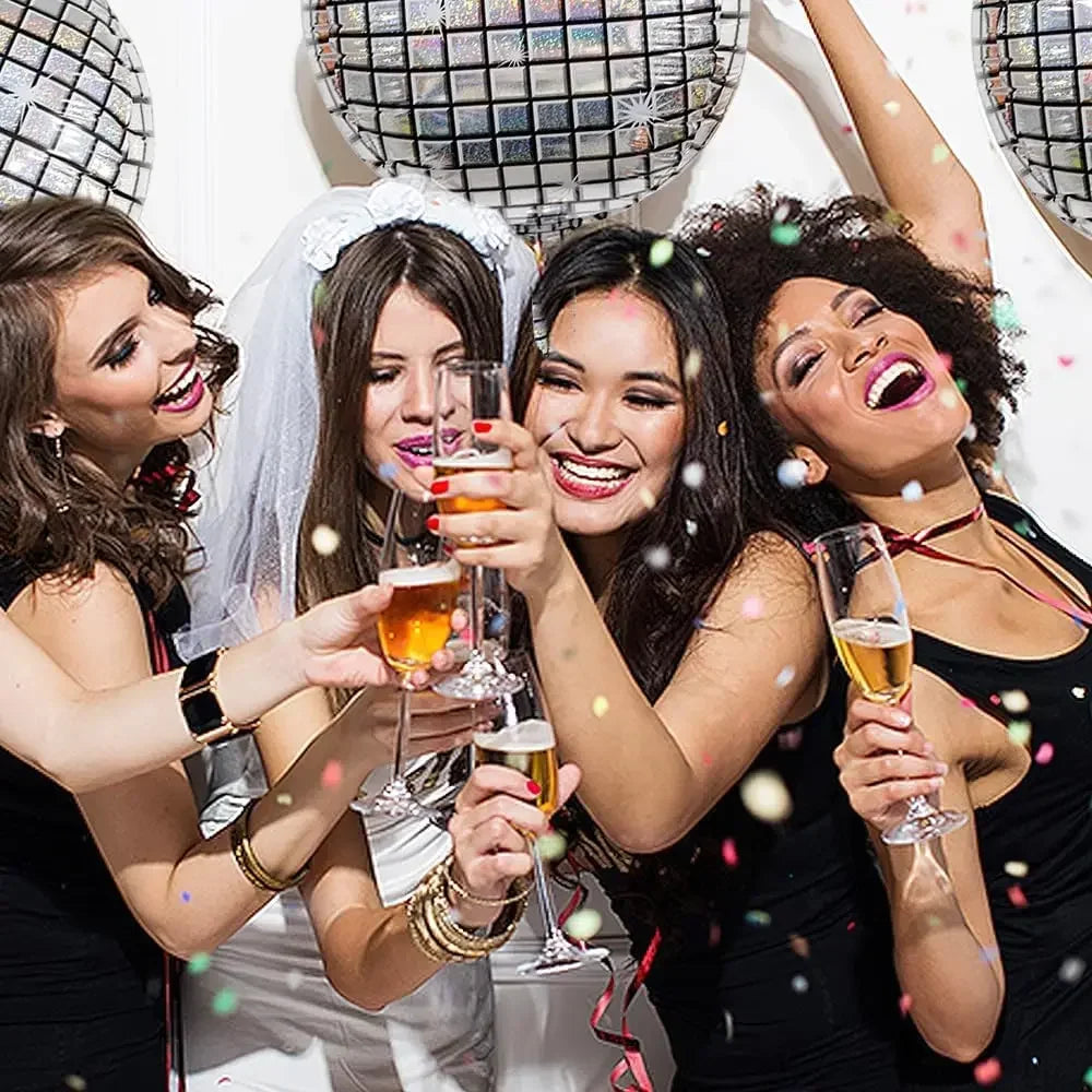 Six women celebrating with drinks and laughing around silver disco ball foil balloons for a birthday party