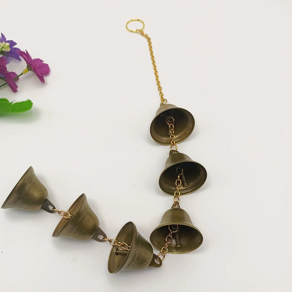 A brass wind chime with multiple bronze bells hanging from a gold chain.