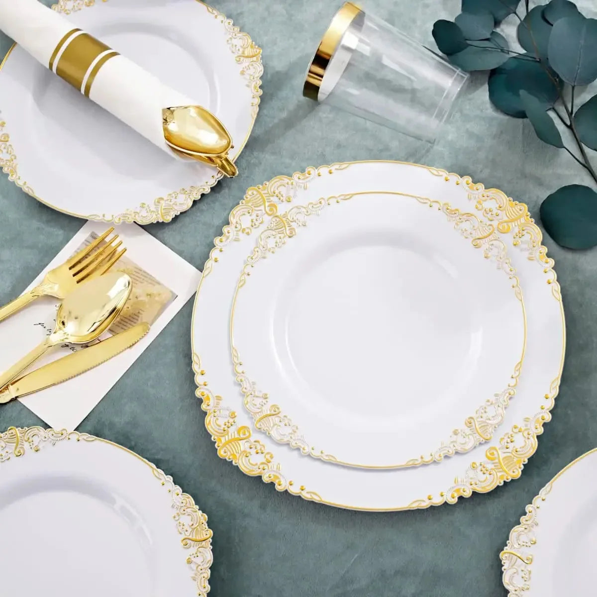 Elegant white and gold disposable dinnerware set featuring plates and cutlery on a gray surface.