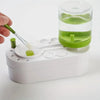 A hand is using a brush to clean a watercolor brush rinser with circulating water inside a clear container.