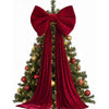 Elegant velvet red Christmas tree topper bow with long streamers decorating a green fir tree.