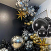 A vertical arrangement of metallic chrome and gold balloons in various sizes and shades against a dark wall.