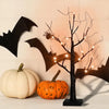 A glowing Halloween birch tree sculpture with LED lights stands next to two pumpkins on a white surface.