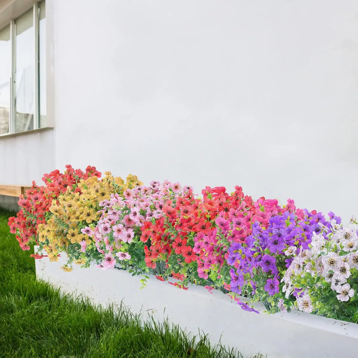 A vibrant bouquet of silk eucalyptus and violet artificial flowers lining a white wall planter.