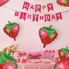 A pink and red themed party decoration featuring a banner, strawberries, and foil balloons.