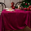 A burgundy red velvet rectangular tablecloth set for elegant dining with festive holiday decorations.
