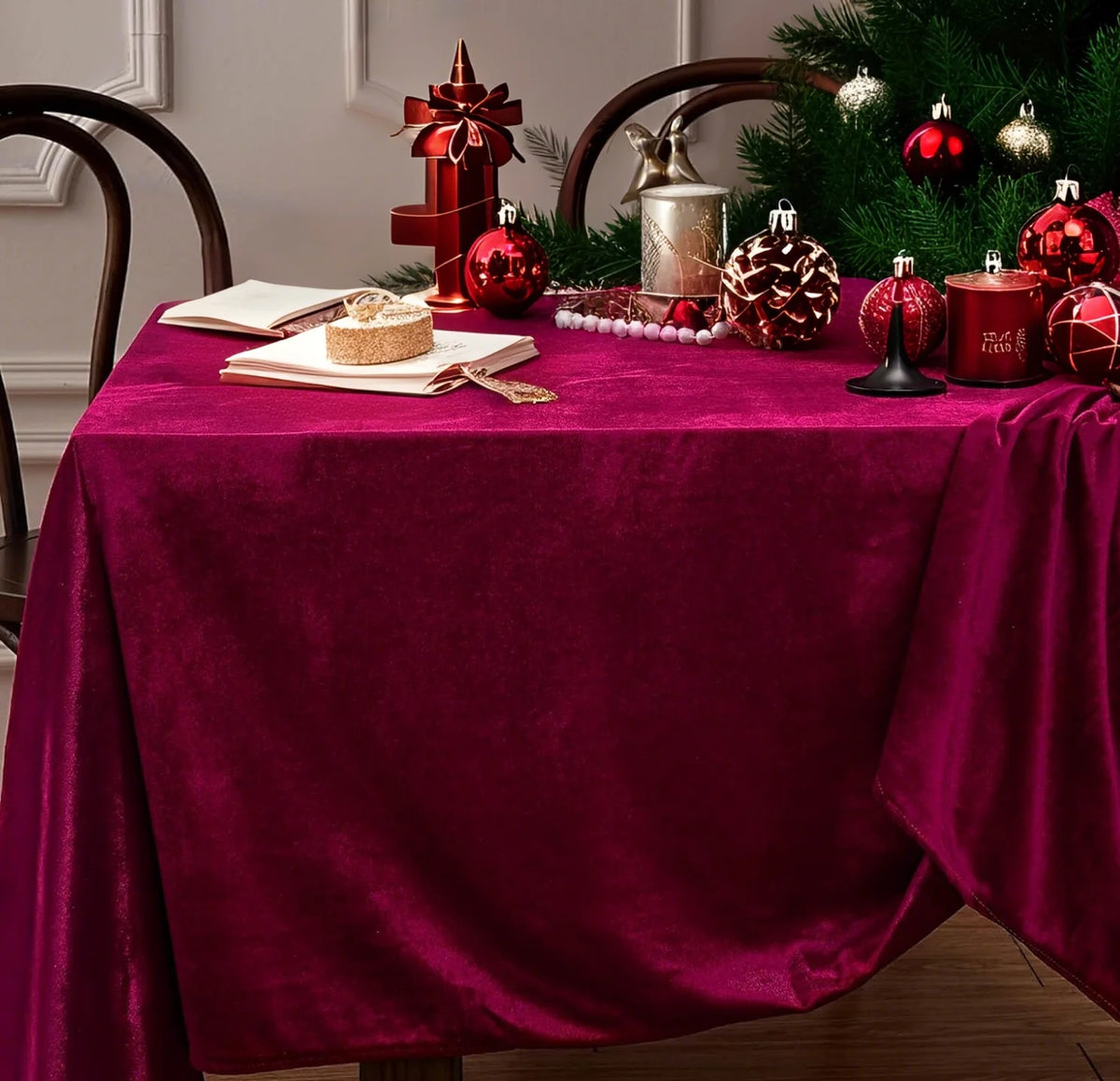 A burgundy red velvet rectangular tablecloth set for elegant dining with festive holiday decorations.