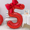 A large red foil number balloon shaped like the number 5 with a matching bow, displayed on a white table.