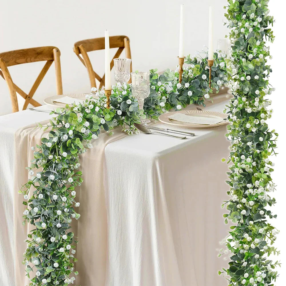 A long, lush green artificial eucalyptus vine garland decorated with white flowers on a draped table setting.