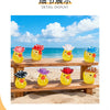 A display of glow-in-the-dark resin duck figurines with colorful hats arranged on a wooden bench outdoors.