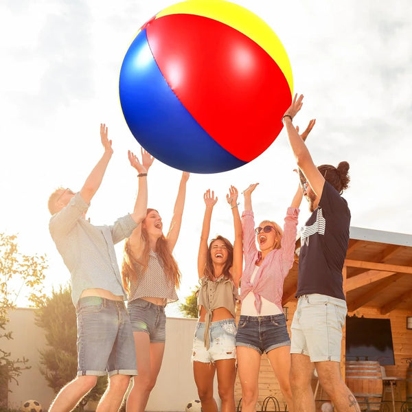 Five young adults are celebrating outdoors while holding a large inflatable pool party ball above their heads.