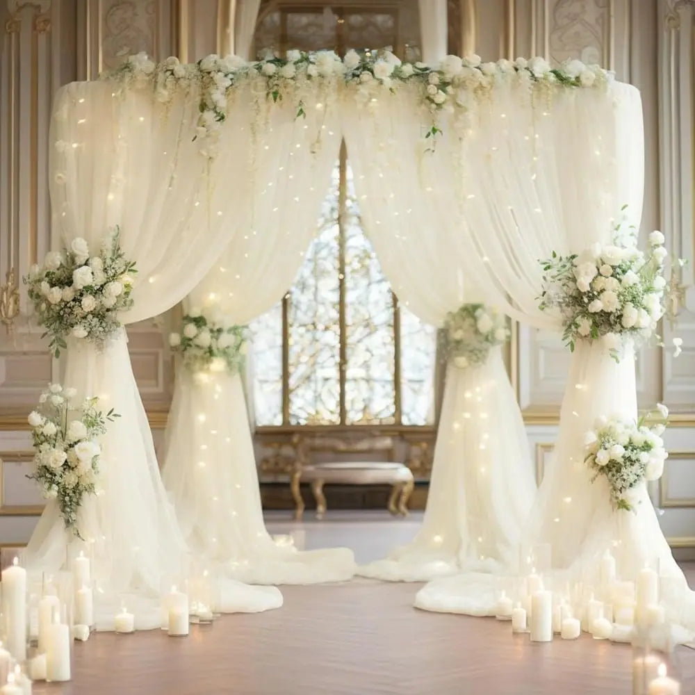 Elegant white wedding tulle backdrop decorated with floral arrangements and twinkling string lights.
