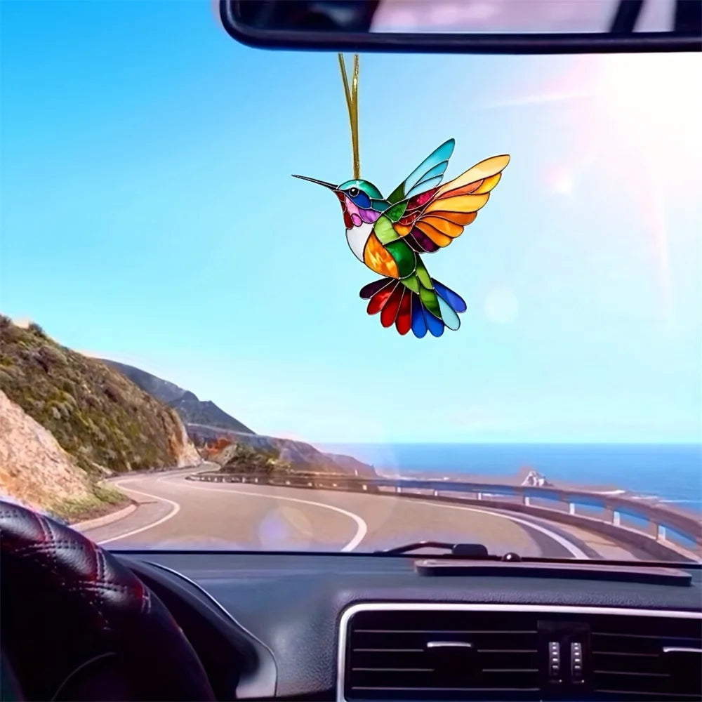Colorful acrylic hummingbird suncatcher hanging ornament suspended in the air against a blue sky and coastline view.