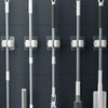 A collection of rod-shaped objects, including mops and brooms, are hung up for storage on a dark gray wall.