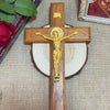 A wooden crucifix with a gold Jesus figure mounted on a cross, set against a beige fabric background.