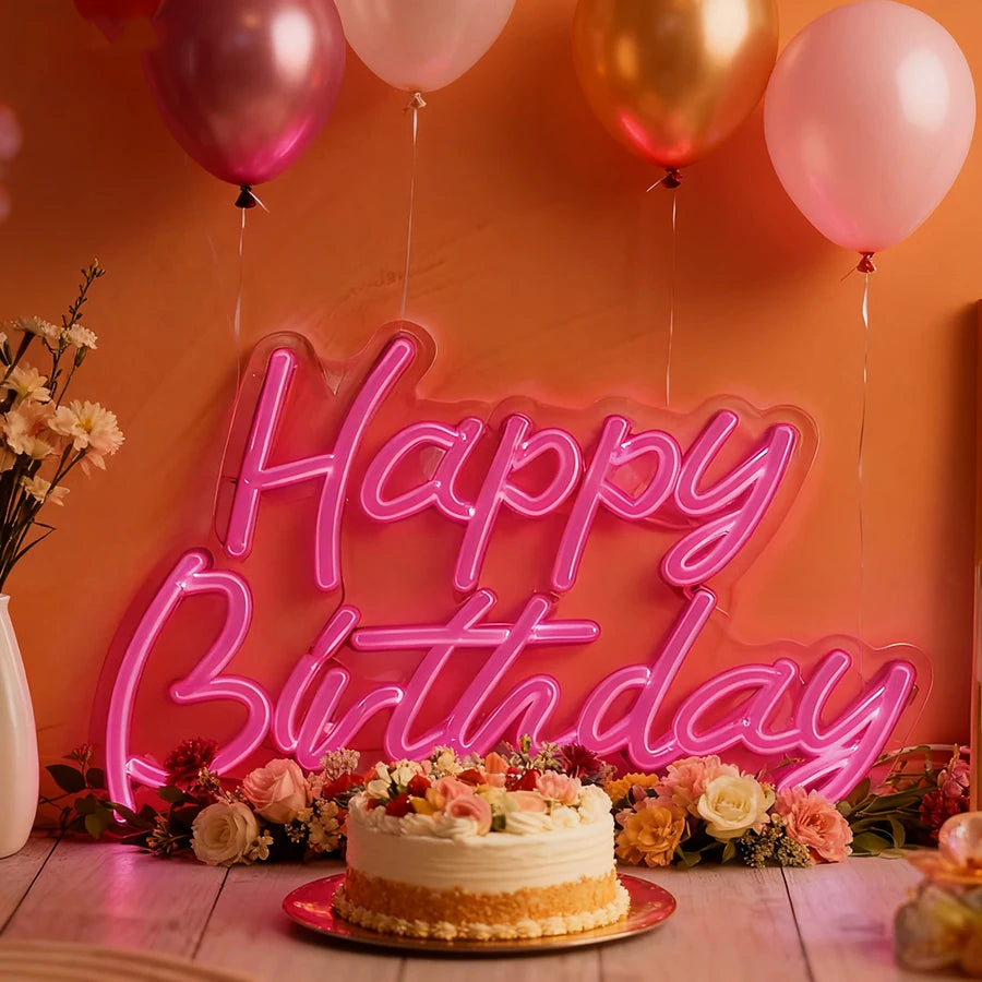 A pink neon wall sign spelling out Happy Birthday with balloons and floral arrangements in an orange setting.