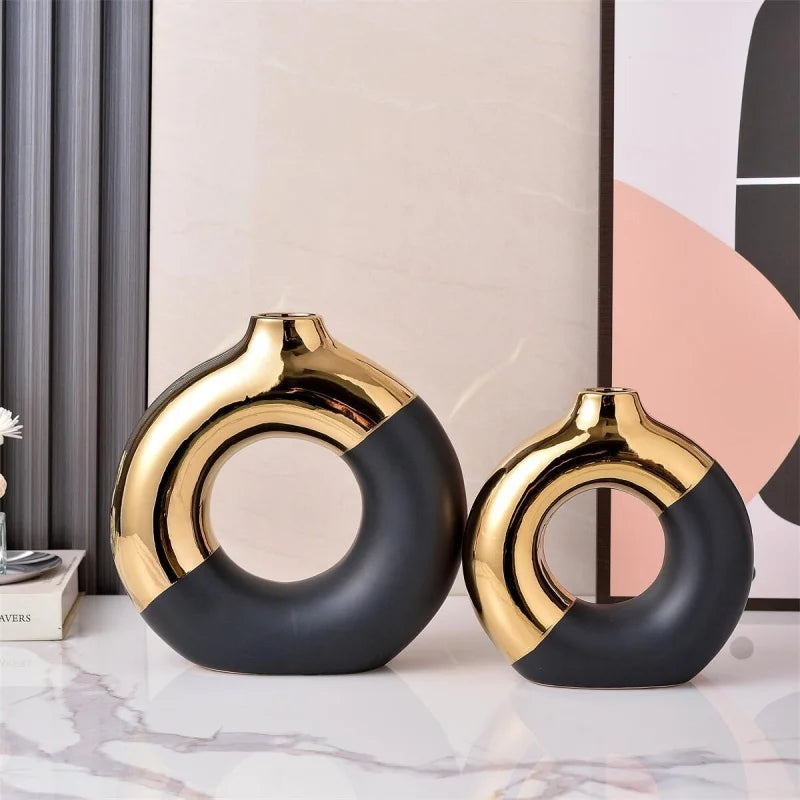 A pair of black and gold ceramic hoop vases displayed on a white marble surface.