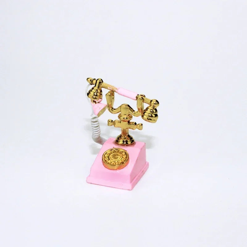 A vintage rotary desk phone miniature decor featuring brass-colored handset and base on a pink stand.