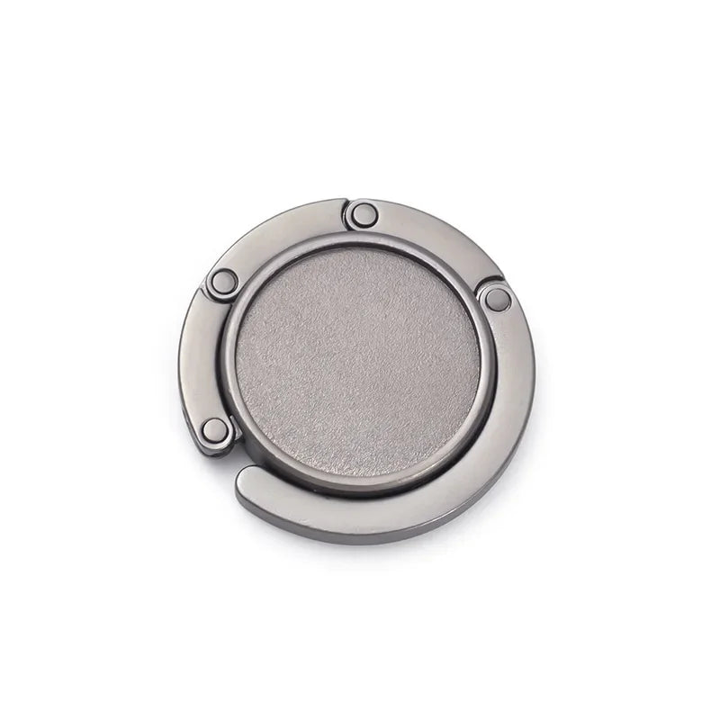 A round, silver-toned compact folding table bag hook or portable purse hanger.