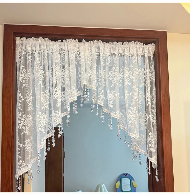 A sheer white beaded lace valance curtain hanging in a wooden frame.