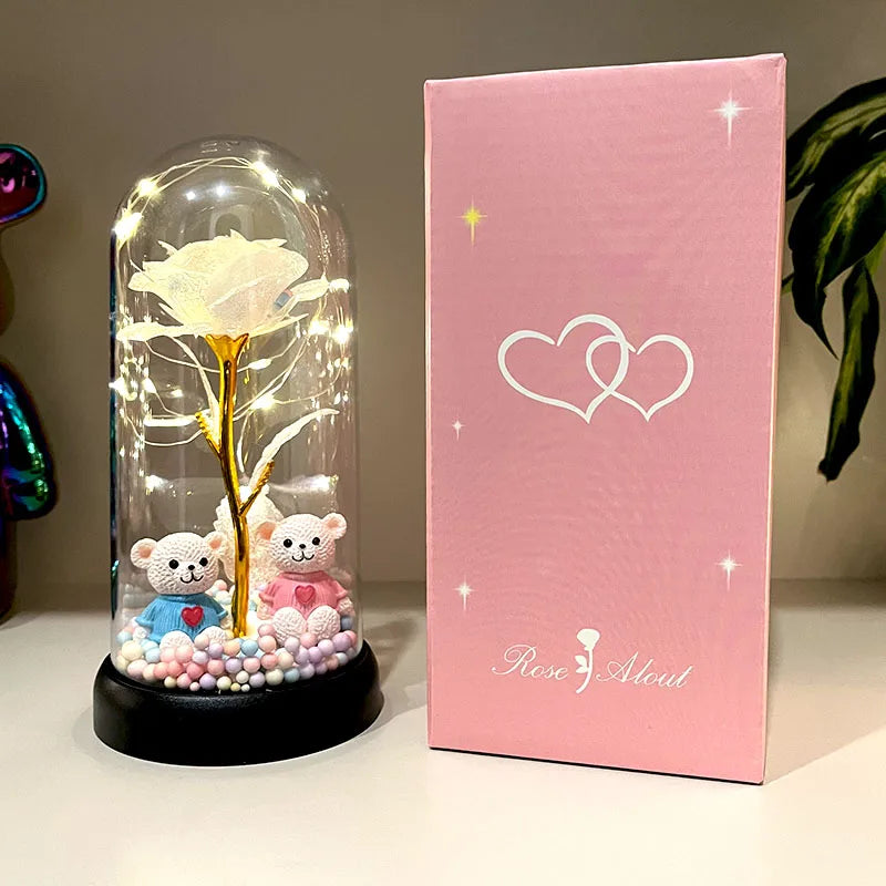 Exhibición de vidrio transparente con una rosa preservada y pequeñas figuras animales blancas y rosas sobre una base negra, j