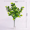 A tall arrangement of green artificial fern and leaf sprigs in a glass vase.