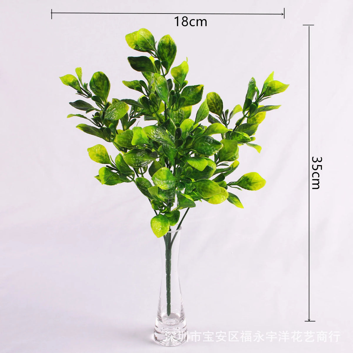 A tall arrangement of green artificial fern and leaf sprigs in a glass vase.