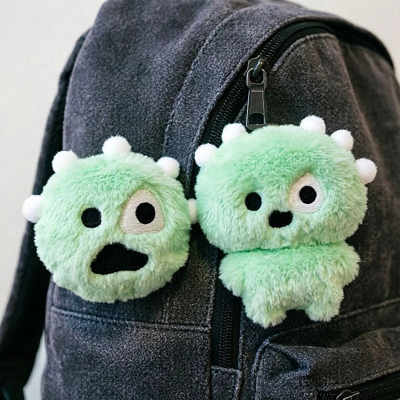 A pair of light green plush keychains with expressive faces are attached to a dark gray backpack.