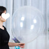 A person holds a large, clear latex balloon against a white curtain backdrop.