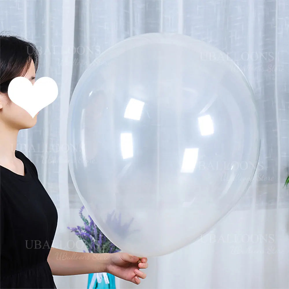 A person holds a large, clear latex balloon against a white curtain backdrop.