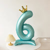 A large, light blue foil balloon shaped like the number six with a gold crown on top.