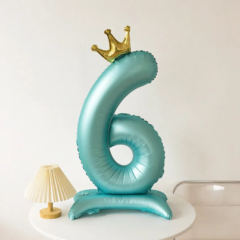 A large, light blue foil balloon shaped like the number six with a gold crown on top.