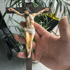 A hand holds a resin sculpture of the Easter Cross crucifix with Jesus on the cross.