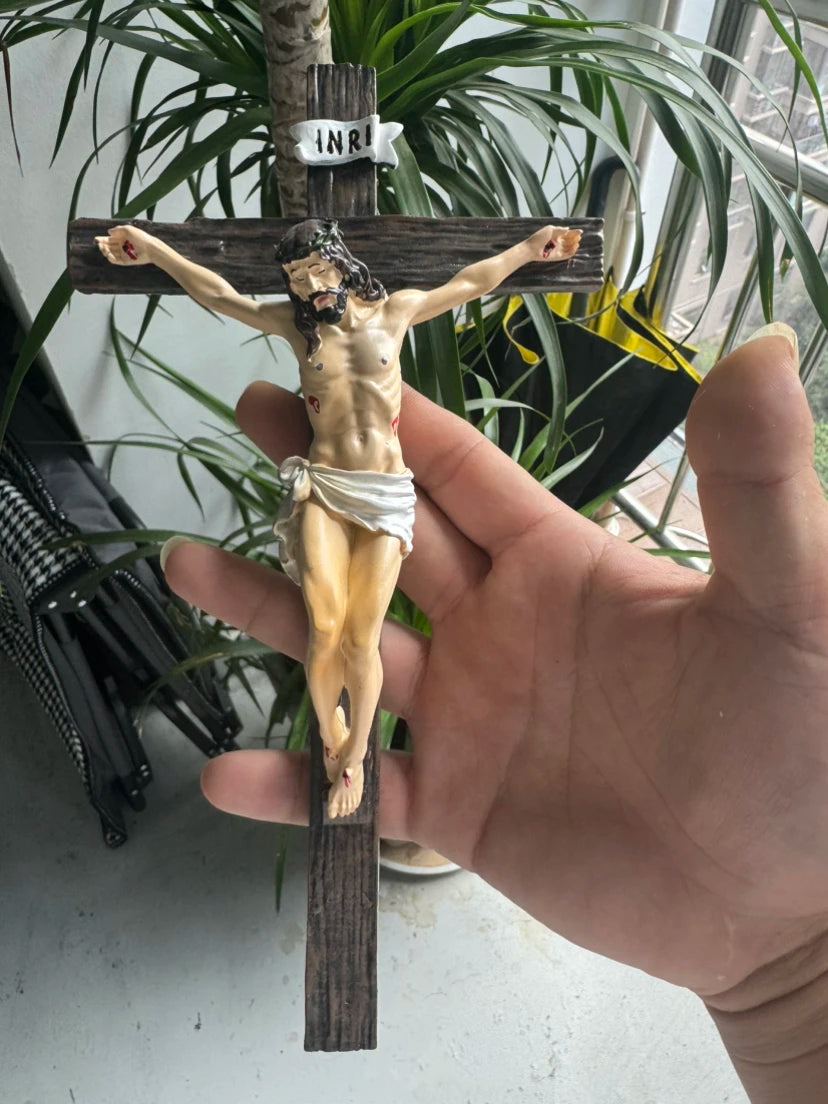 A hand holds a resin sculpture of the Easter Cross crucifix with Jesus on the cross.
