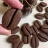 A hand holds a dark brown coffee bean cookie stamp mold with a visible crease, surrounded by other similar cookies.