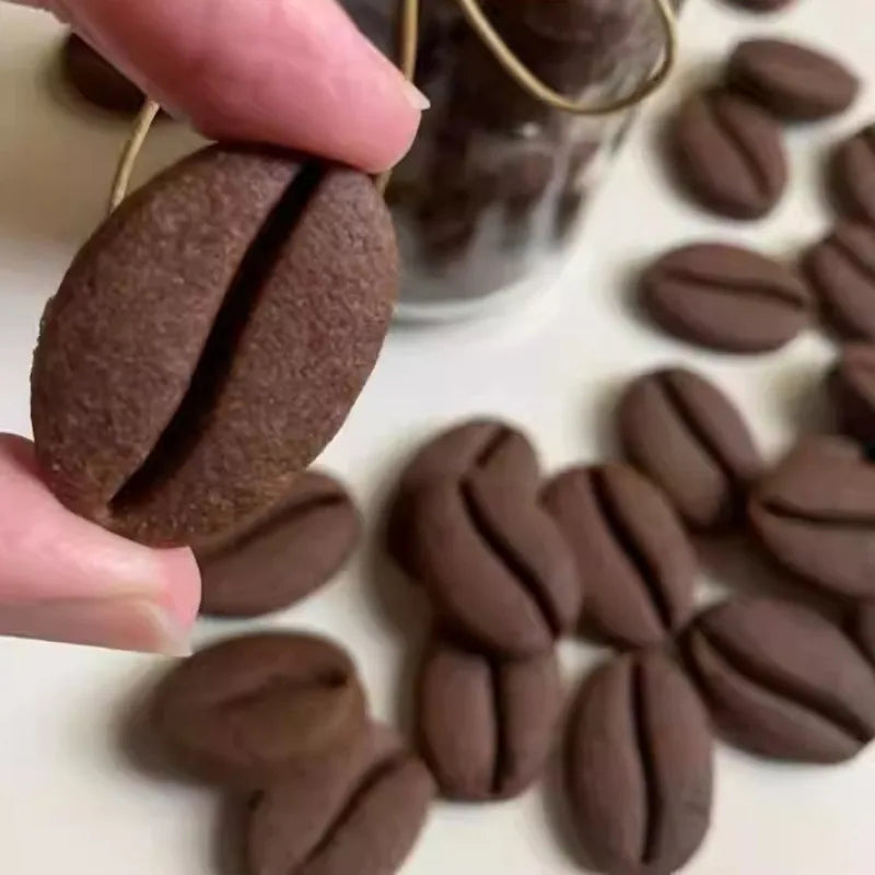 A hand holds a dark brown coffee bean cookie stamp mold with a visible crease, surrounded by other similar cookies.