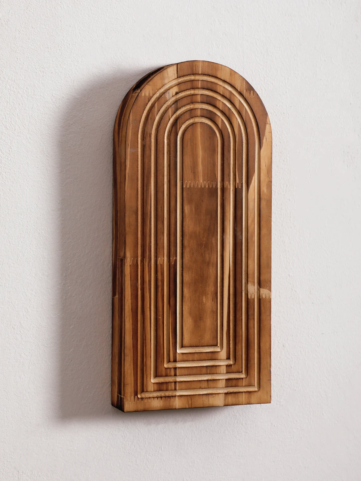 Jarrón de pared arqueado de madera vertical con estrías concéntricas y acabado texturizado sobre una pared blanca.