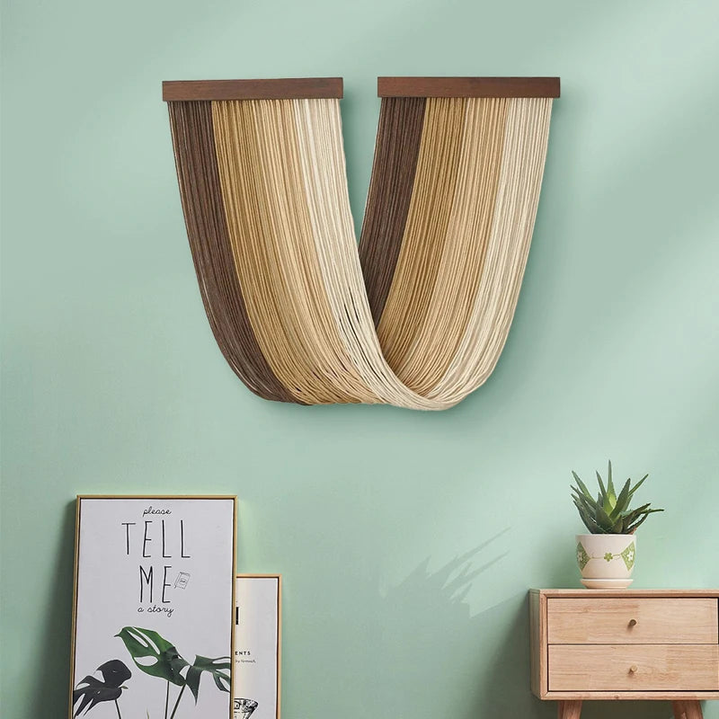 Boho macrame wall tapestry featuring vertical stripes of beige, brown, and cream tones mounted on a light green wall.