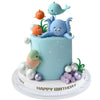 A light blue cake decorated with sea animal toppers, including a dolphin and a turtle, surrounded by pearl balls.