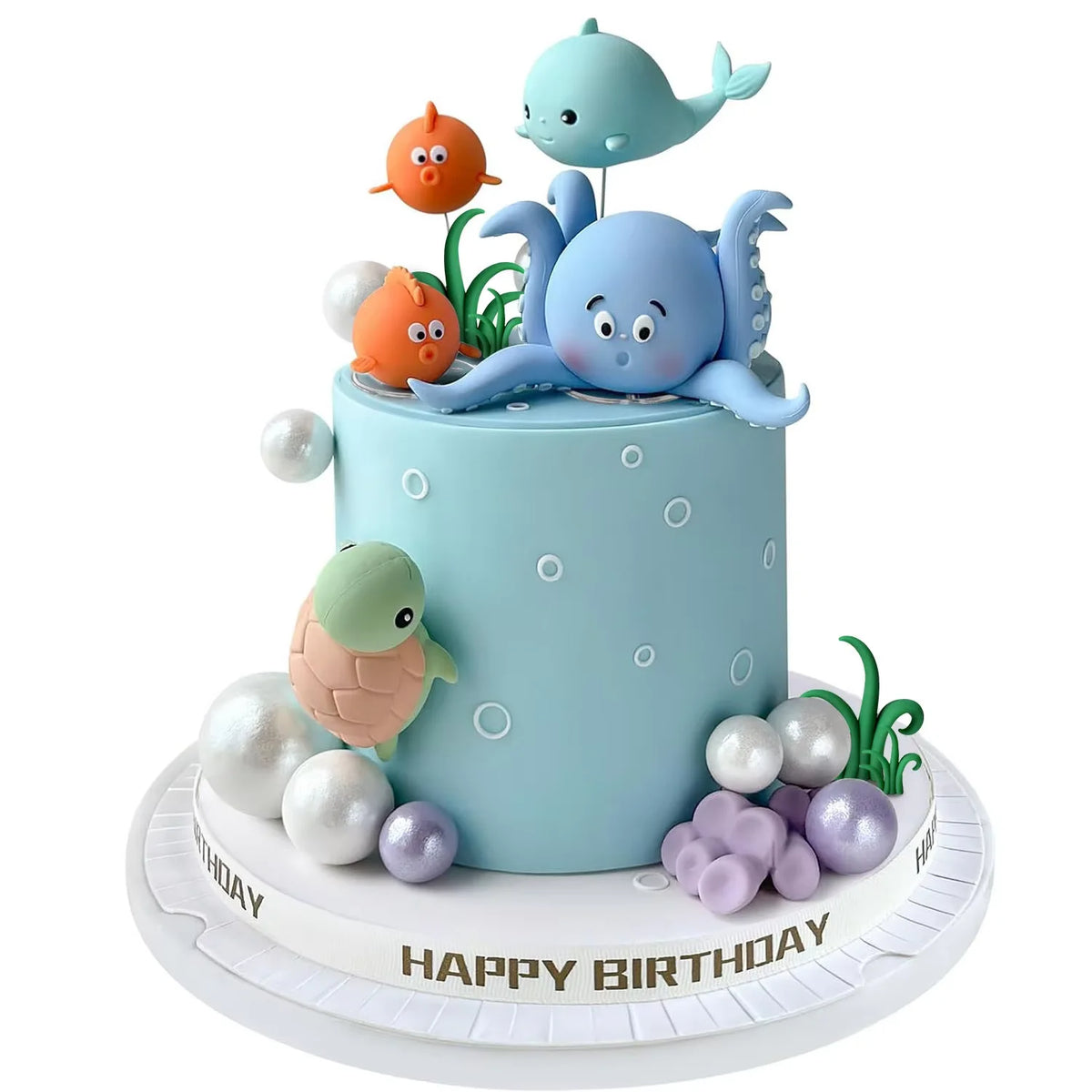 A light blue cake decorated with sea animal toppers, including a dolphin and a turtle, surrounded by pearl balls.