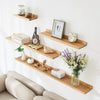 A set of natural wood floating shelves mounted on a white wall displaying various decorative items and books.