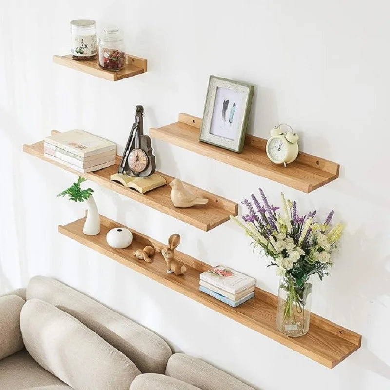 A set of natural wood floating shelves mounted on a white wall displaying various decorative items and books.